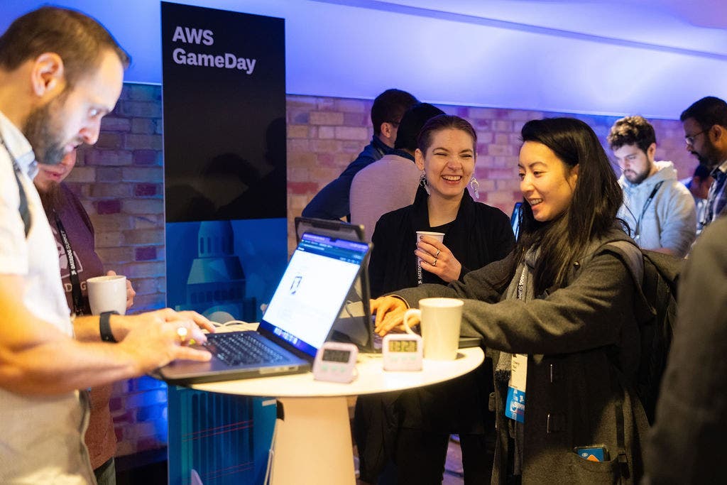 People stand at elevated tables and use their laptops to participate in AWSGameDay.