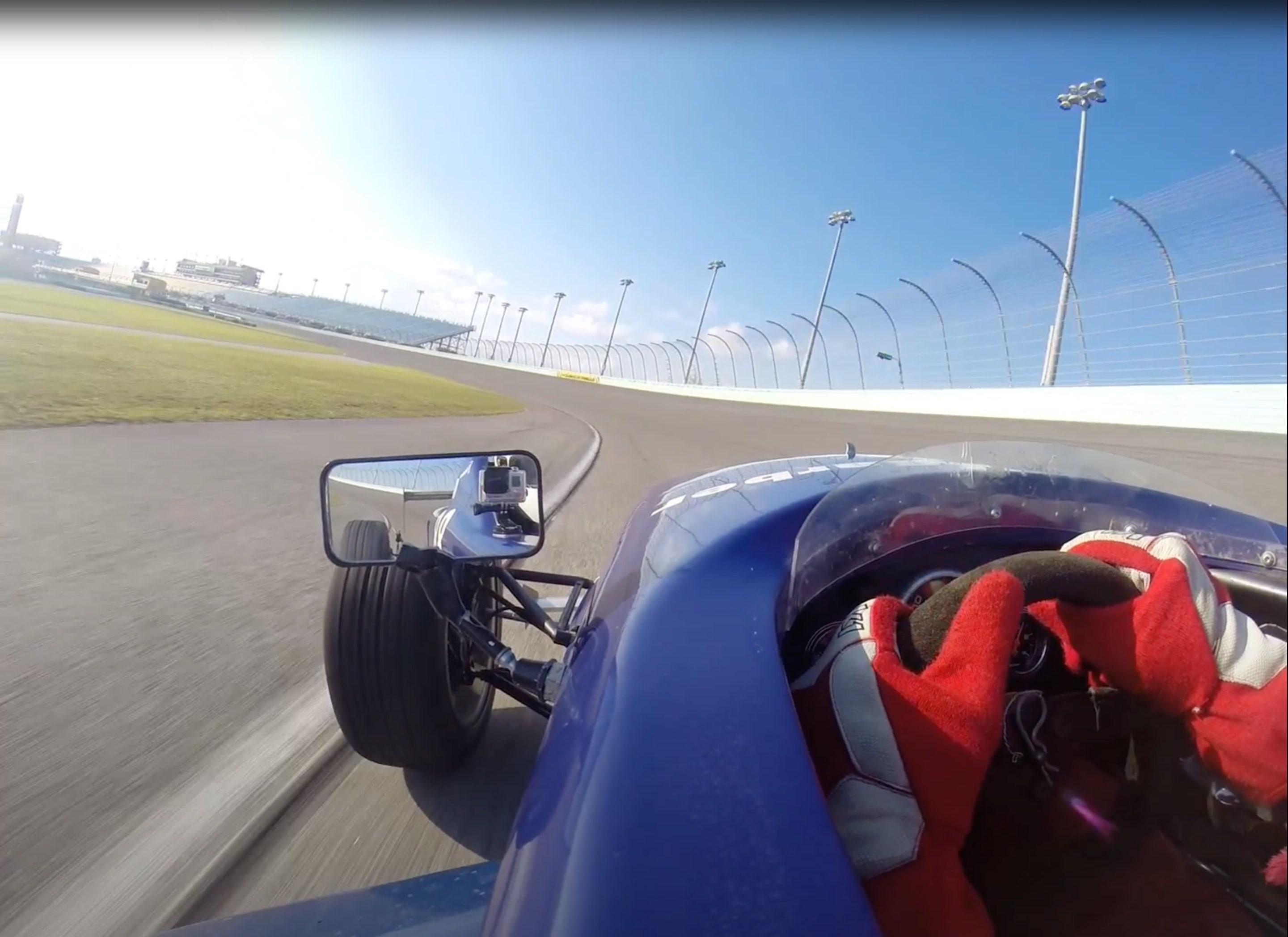 Photograph looking out of a race car, with a view of the track and of the side mirror.