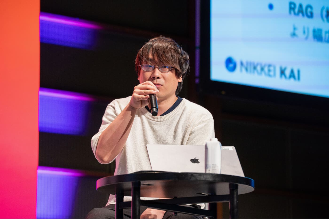 ステージ上でマイクを持って話す日本経済新聞社の若原義隆。 ステージ上でマイクを持って話す日本経済新聞社の若原義隆。